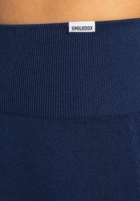 Navyblå ribbad midjeband på leggings med en slät textur. Har en liten vit "SMILODOX"-etikett på baksidan.