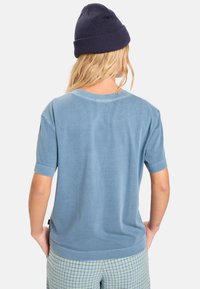 Pamutból készült, világoskék rövid ujjú póló. Kerek nyakkivágással és mandzsettás ujjal rendelkezik, zöld és kék kockás nadrággal párosítva.