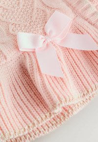 Helles rosa Strickmütze mit Zopfmuster, verziert mit einer glatten rosa Schleife und einem metallischen goldenen Akzent am unteren Rand.