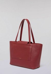 Czerwona torba na ramię ze skóry o stabilnym kształcie, z podwójnymi uchwytami i przednią kieszenią. Powierzchnia ma gładką fakturę i subtelny połysk.