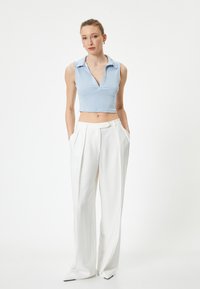 Top corto de color azul claro con cuello y escote en V, combinado con pantalones blancos de tiro alto y con pliegues, creando una silueta limpia y moderna.