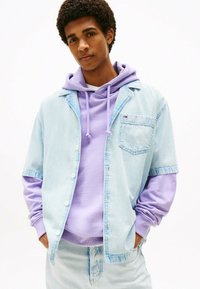 Jasnoniebieska dżinsowa koszula z krótkim rękawem na fioletowym hoodie. Koszula ma kieszeń i białe guziki, a hoodie ma sznurki do regulacji.