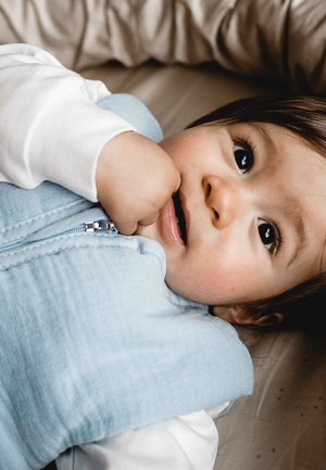 Hellblaues ärmelloses Babyweste aus strukturiertem Material, mit einem Reißverschluss vorne und einem weißen Langarmshirt darunter.
