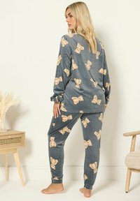 Harmaa pyjama-setti, joka on valmistettu pehmeästä kankaasta ja jossa on ympäriinsä teddykarhukuosi. Pitkähihainen paita on rentoa mallia ja siinä on ribbireunat.