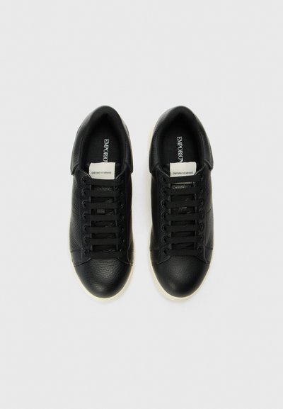 Svarta lädersneakers med strukturerad ovandel, slät tåhätta och vita gummisulor. Har svarta snören och ett varumärkesmärke på tungan.