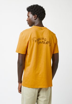Korte mouwen gele t-shirt met de tekst "FISHING THERAPY!" in het zwart op de rug; gladde textuur en relaxte pasvorm.