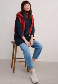 Tunique en denim foncé superposée sur un col roulé à rayures rouge, accompagnée de jeans cropped bleu clair et de baskets gris-blanc.