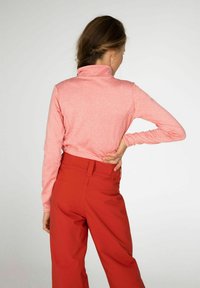 Langermige top met hoge kraag van lichtroze stof, gecombineerd met rode high-waisted broek. Soepele textuur, getailleerd ontwerp en minimale details.