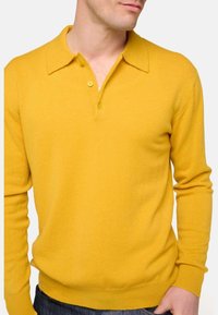 Gelbes Strick-Polo-Shirt mit Kragen, zwei Knöpfen und gerippten Bündchen. Weicher Stoff und taillierte Passform.