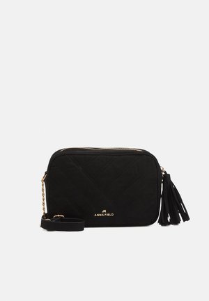 Schwarze gesteppte Umhängetasche mit goldener Kette, Quasten-Details und "ANNA FIELD" Logo vorne.