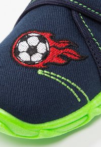 Marineblauwe stoffen schoen met groene zool; beschikt over een rode en zwarte vlam-geborduurde voetbaldessin; contrasterende stiksels.