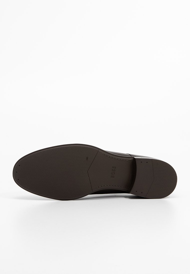 Semelle de chaussure en cuir marron avec une surface texturée, comportant de petits motifs de grip et le nom de la marque "BOSS" en relief près du talon.