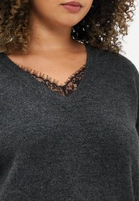 Suéter de malha cinza escuro com um decote em V adornado com uma delicada renda preta na gola, textura suave e corte ligeiramente folgado.