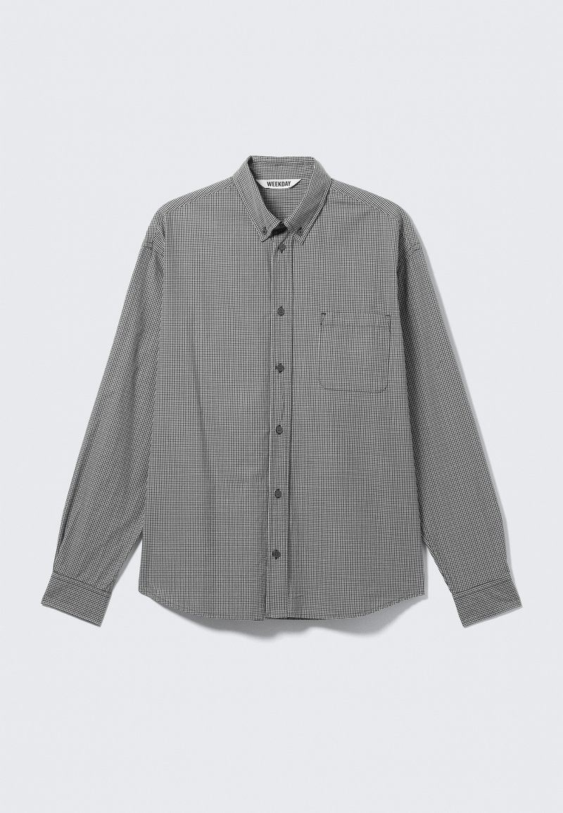 Chemise à manches longues à petits carreaux noirs et blancs, à boutons, avec col et poche poitrine, étalée à plat sur un fond clair.