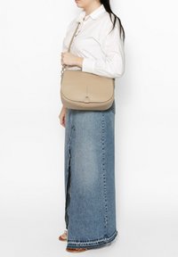 Sac à épaule en cuir beige avec un rabat incurvé, surface texturée et un détail de couture décoratif. La bandoulière ajustée pend de manière diagonale.