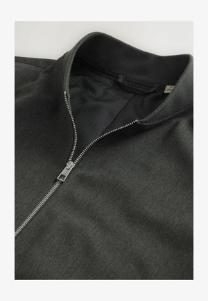 Giacca nera con zip e una superficie testurizzata, colletto a maglia piatta e zip argentata. L'interno presenta un tessuto a rete per favorire la traspirabilità.