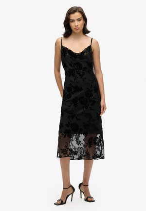 Vestido de terciopelo negro con estampado floral y acabado satinado, que presenta un escote drapeado y tirantes finos ajustables, complementado con un dobladillo transparente.