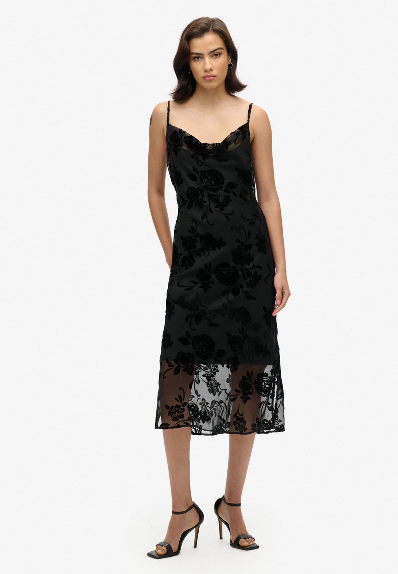 Robe en velours noir à motifs floraux avec une finition satinée, dotée d'un col drapé et de bretelles spaghetti réglables, agrémentée d'un ourlet transparent.