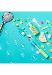 Pommeau de douche, gel douche vert, jouets colorés, articles pour bain moussant et petits accessoires en plastique disposés sur un fond turquoise avec des bulles.