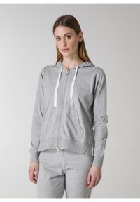 Grå zip-up hoodie i ett mjukt tyg, har ett fodrat huva, kontrasterande snören och framfickor. Matchas med matchande grå byxor.