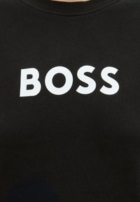Tissu noir avec un texte blanc en majuscules et en gras "BOSS" centré sur la surface.
