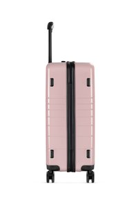 Valigia rigida di colore rosa chiaro con una superficie testurizzata, cerniera nera e manico estensibile. Quattro ruote nere per la mobilità.