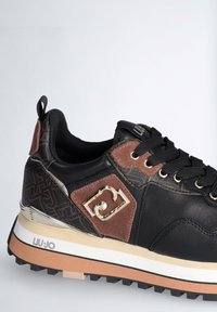 Sneaker nero e marrone con tomaia in pelle texturizzata, dettaglio in metallo dorato e design decorato sul tallone. Suola in gomma per una migliore trazione.