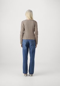 Beige strikket genser med et teksturert mønster, tettsittende i midjen. Kombinert med høyt liv blå denimjeans, som er litt utsvingte i kanten.