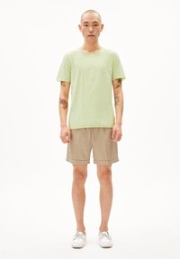 Helles grünes kurzärmeliges T-Shirt aus Baumwolle, kombiniert mit beigen Shorts. Auffällige Details sind der umgeschlagene Saum der Shorts und lässiges Schuhwerk.