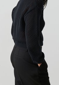 Marineblauer Strickpullover mit einem strukturierten, offenen Design. Hat einen gerippten Saum und Ärmelbündchen. Kombiniert mit eleganten schwarzen Hosen.