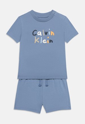 Gyerek kék rövid ujjú ing és rövidnadrág szett, a póló elején több színű "Calvin Klein" felirattal és egy gombbal a vállán.