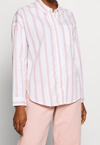 Striped button-up shirt with light pink and white vertical stripes, featuring long sleeves and a chest pocket. Cotton material, casual fit.