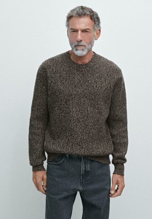 Brown textured sweater with a round neckline and long sleeves, paired with gray jeans. The fabric features a mixed pattern.