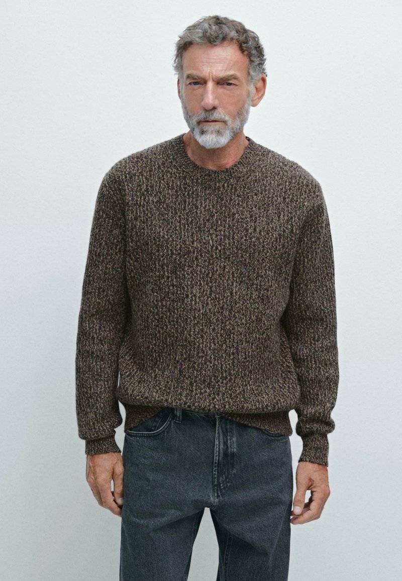 Bruine gestructureerde trui met een ronde halslijn en lange mouwen, gecombineerd met grijze jeans. De stof heeft een gemengd patroon.