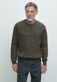 Brązowy sweter o fakturze z okrągłym dekoltem i długimi rękawami, połączony z szarymi dżinsami. Tkanina ma mieszany wzór.