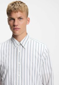 Witte overhemd met verticale marineblauwe strepen, voorzien van een klassieke kraag en gladde katoenen stof, gedragen door een model met kort, textuur haar.