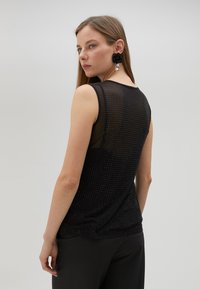 Svart ärmlös topp med en strukturerad design som har små perforeringar. Slätt tyg med en något genomskinlig känsla.