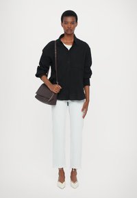 Camisa negra de botones, jeans desgastados azul claro, tacones blancos puntiagudos, llevando un bolso de hombro de cuero marrón con cierre de solapa.