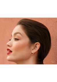 Boucle d'oreille en argent avec un petit détail d'accent, sur fond pêche texturé. Le profil du modèle met en valeur le design de la boucle.