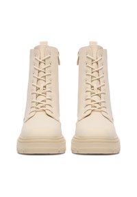 Beżowe botki do kostek o gładkiej fakturze, z przodem na sznurówki, zamkiem błyskawicznym z boku oraz grubą, żłobioną podeszwą.
