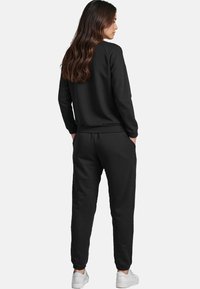Svart sweatshirt och joggers, tillverkade av ett mjukt tyg. Joggers har en elastisk midja och åtsittande muddar. Vita sneakers fulländar looken.