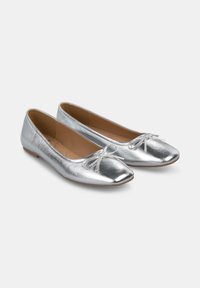Ballerines argentées avec un éclat métallique, bout carré et un nœud décoratif à l'avant. Texture lisse, semelle à profil bas.