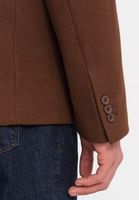 Brun ullblazer med en strukturerad yta, i slim fit, med detaljer som treknappsmanschetter och en något avsmalnande midja.