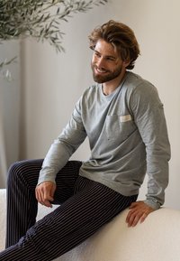 Grijs langwaardig shirt met een borstzak, gecombineerd met marineblauwe en witte gestreepte pyjamabroek, zittend op een licht gestructureerd oppervlak.