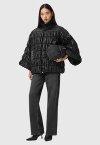 Svart vadderad jacka med hög krage, med en texturerad yta och veckad design. Kombinerad med mörkgrå vida jeans och svarta stövletter med klack.