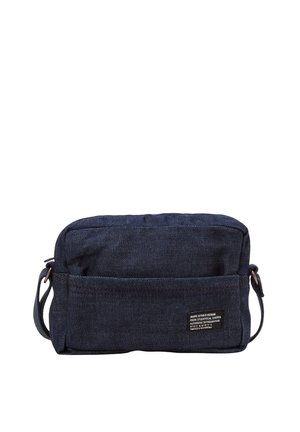 Sac bandoulière rectangulaire en denim bleu foncé avec poche avant et sangle réglable, avec une petite étiquette de marque noire et blanche.