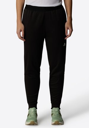 Black tapered sweatpants with elastic waistband and cuffs, worn with light green running shoes on a white background.