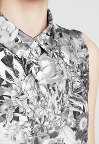 Bezrukávová halenka s květinovým černo-bílým vzorem. Má límec a zapínání na knoflíky, vyrobená z lehké látky.