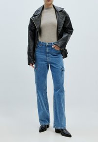 Zwarte leren motorjack, beige aansluitend topje, hooggeprijsde blauwe cargo jeans en zwarte puntige enkelschoenen.