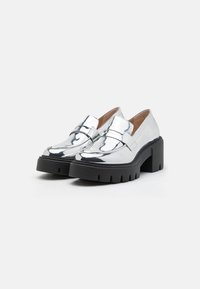 Sølvmetallic loafers med en chunky sort platform heel. Glat, skinnende overflade med en dekorativ rem tværs over toppen.